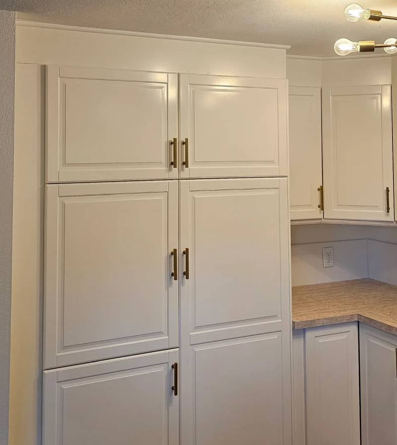 White kitchen cabinets with gold handles in a corner, with a light fixture and counter visible.
