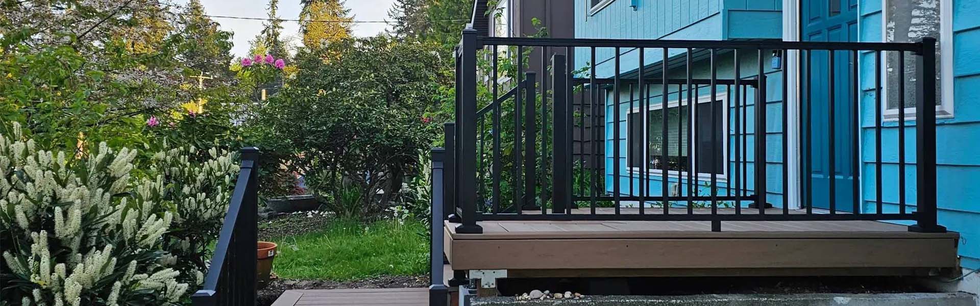 Brown composite steps and deck with black railings leading to a turquoise house surrounded by green foliage.