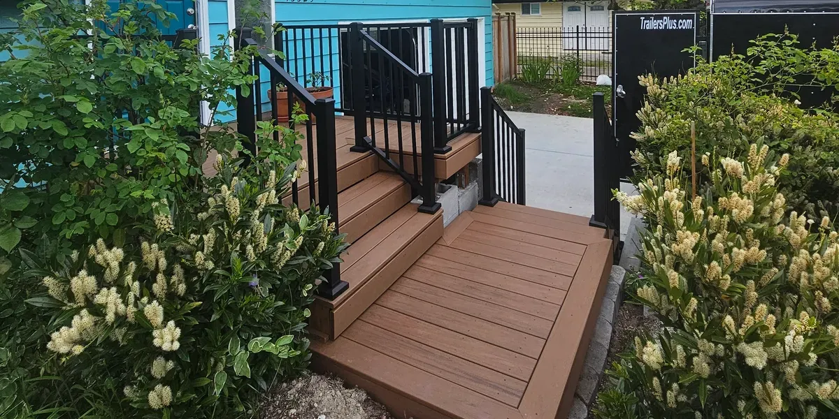 Brown composite deck with black railings and stairs leading to a light blue house